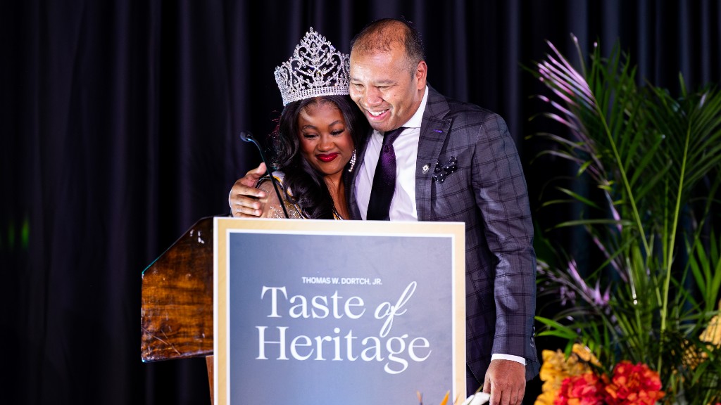 A crowned honoree embraced on the Taste of Heritage stage